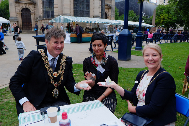 Manaz sits at an outdoor table with the Lord Mayor who shows off the teabag he's made.