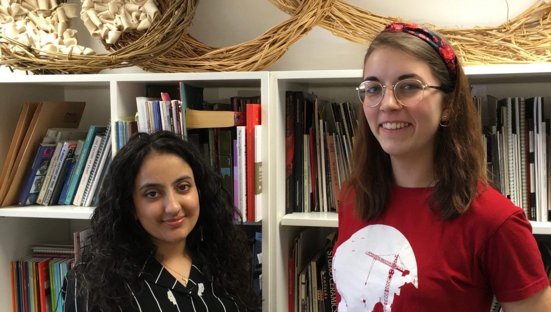 Daljinder and Hayley stand smiling in front of a bookcase