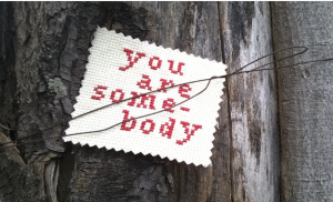 A stitched affirmation saying 'You Are Somebody', tied to a tree. 